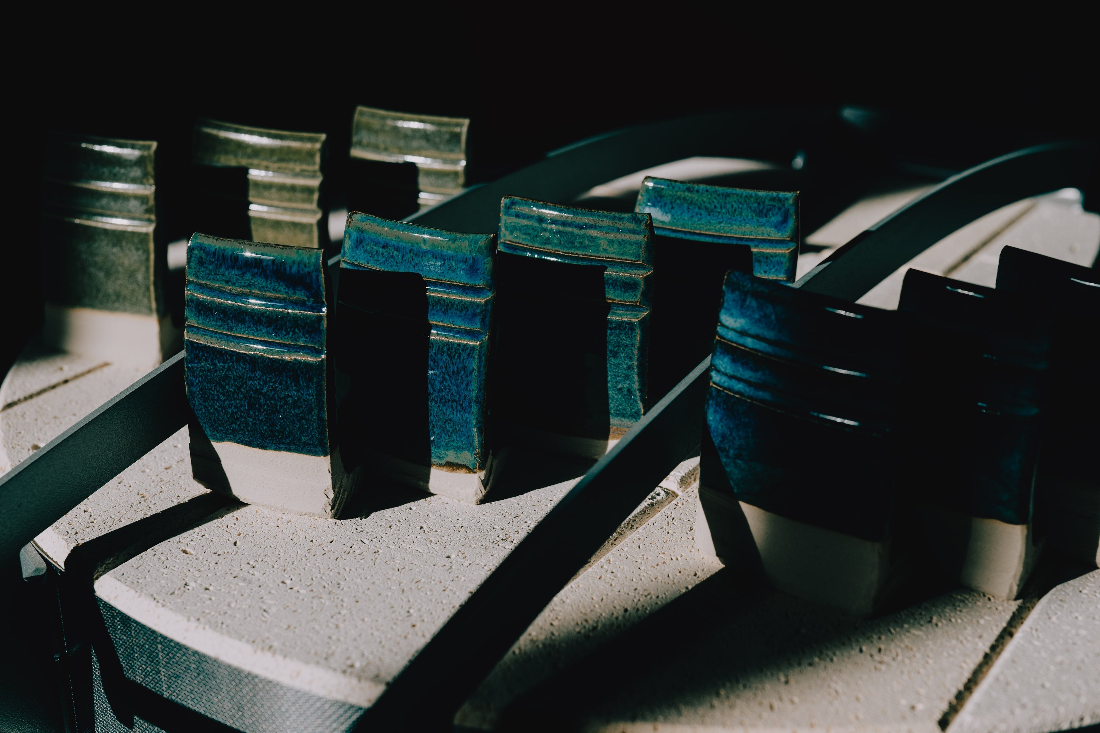 Close-up of ceramic test tiles with layered blue and white glazes arranged on a kiln shelf under soft studio lighting.