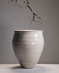 Gray ceramic vase on a gray surface with a branch above it