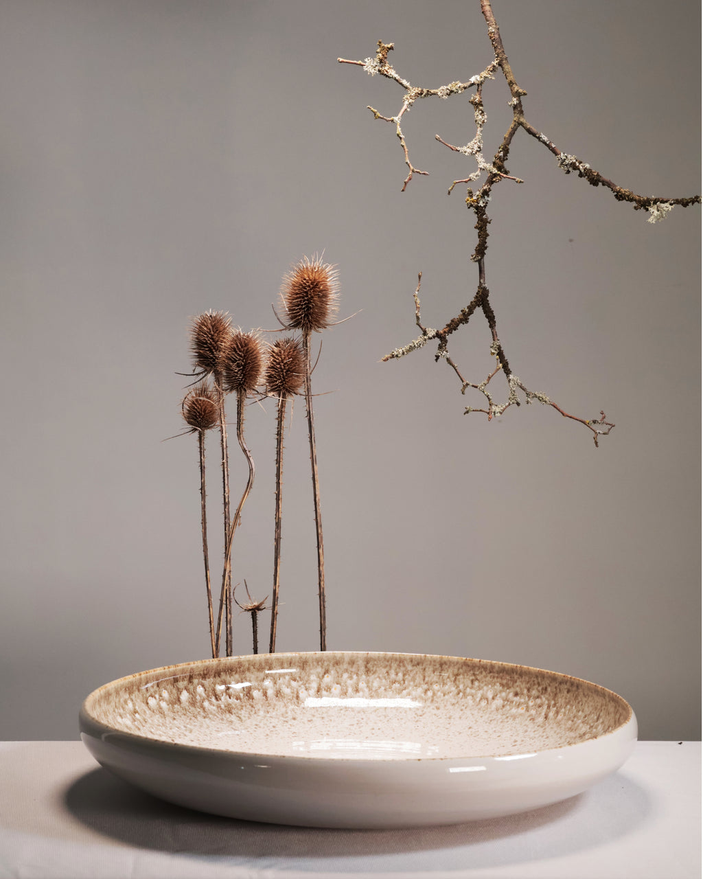 White ceramic bowl with textured rim on a gray surface, containing dried plants against a neutral background.