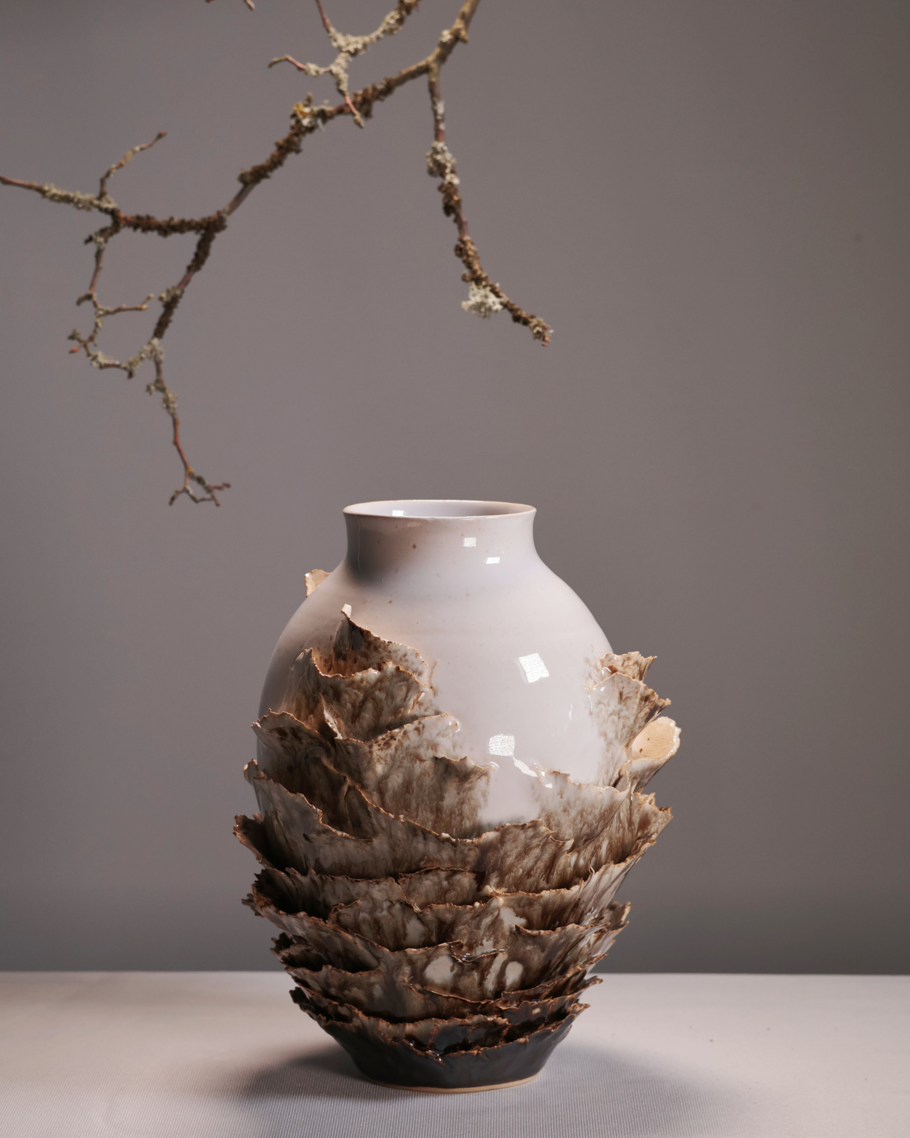 Vase with layered design and natural elements on a gray background