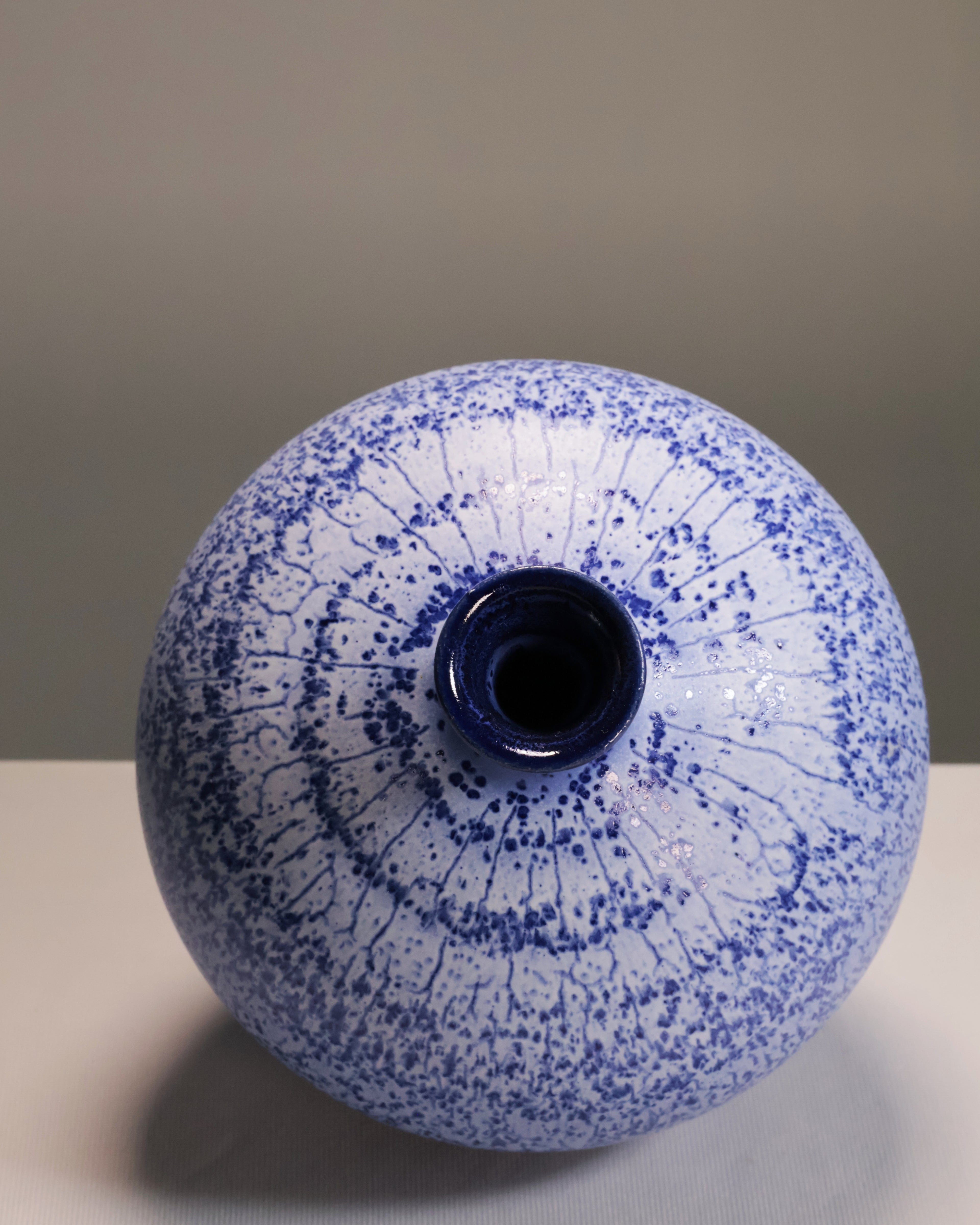 Ceramic vase with blue speckled pattern on a neutral background