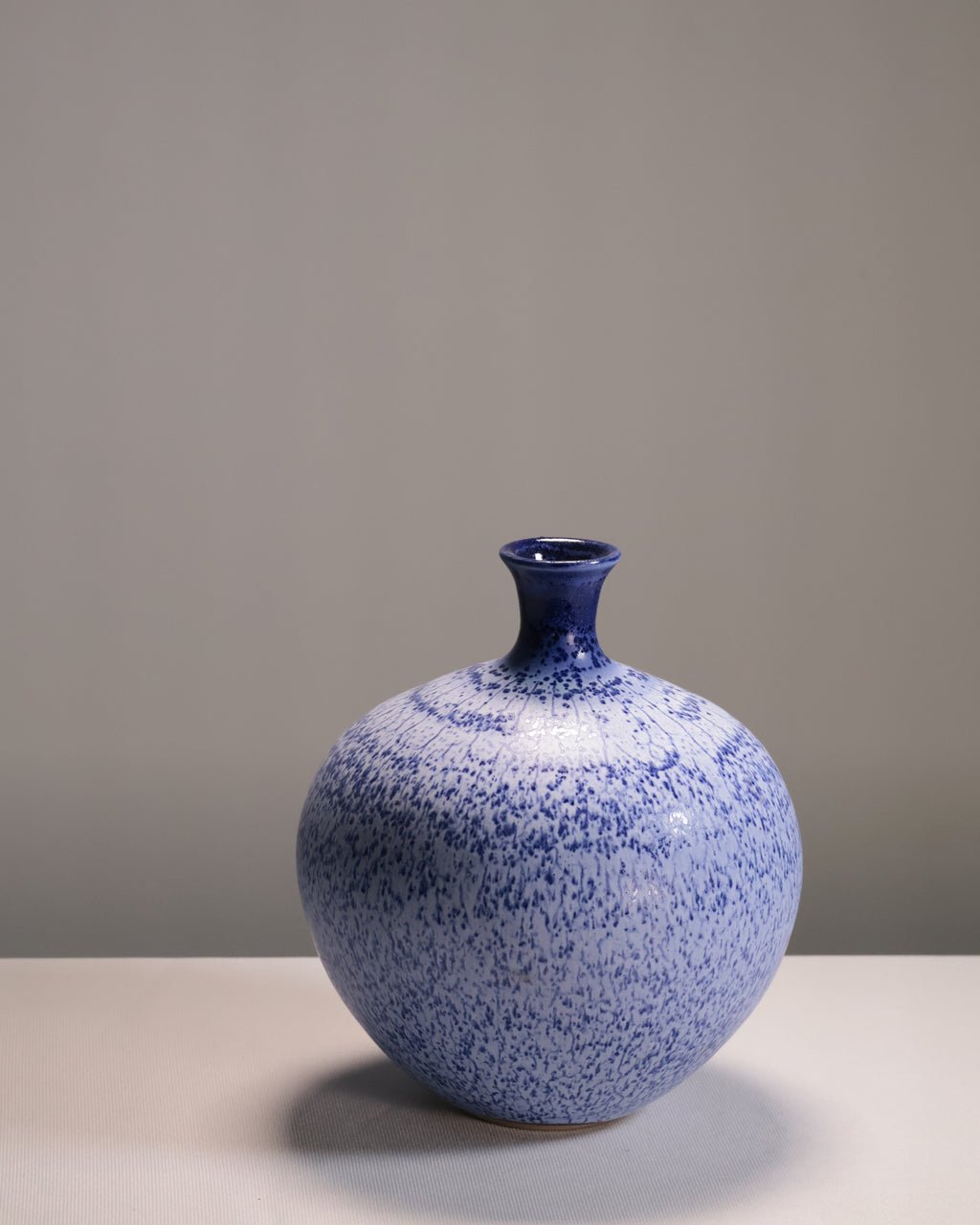 Blue speckled vase on a gray surface with a gray background