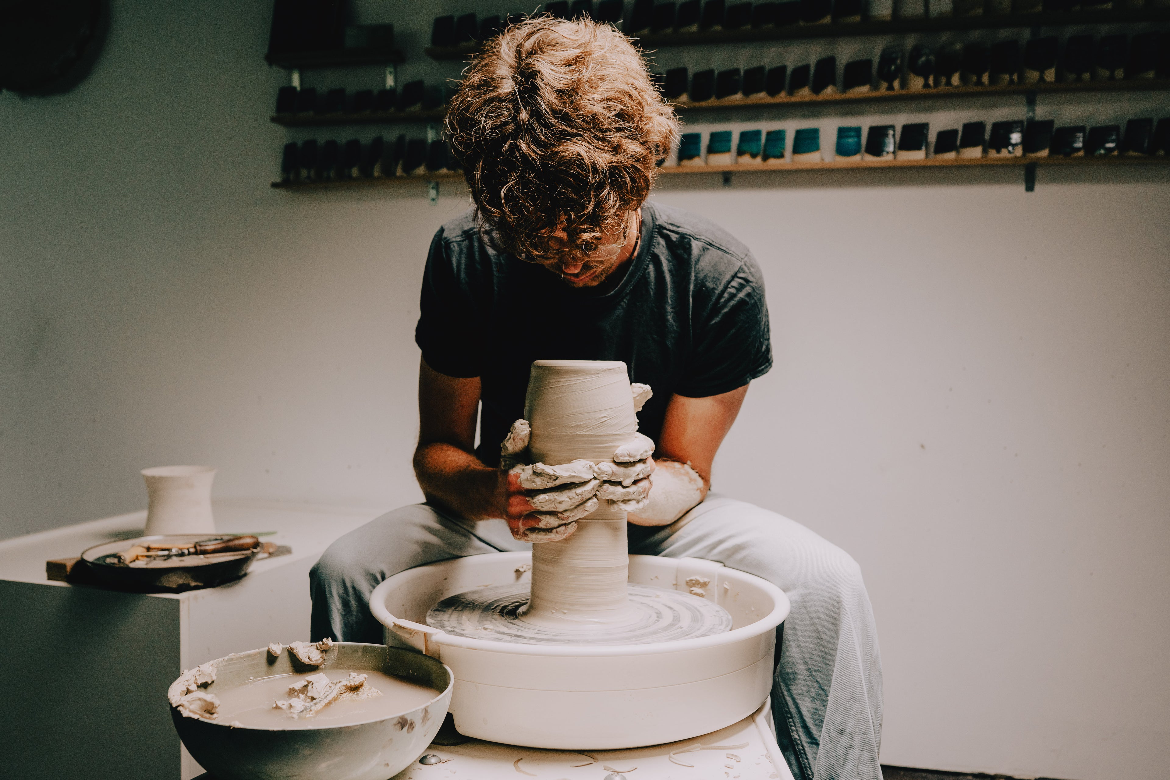 Person working with clay on a pottery wheel in a studio setting