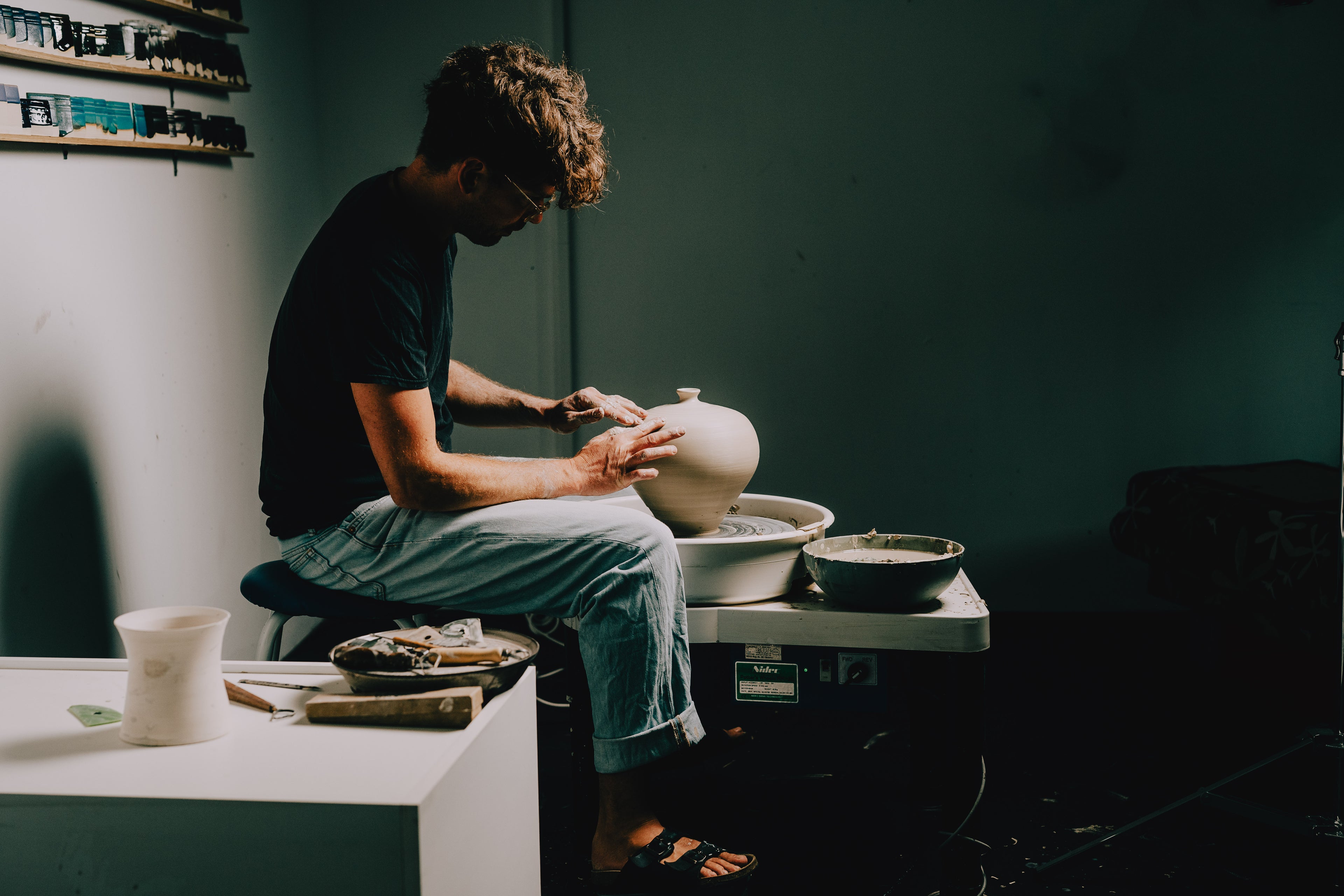 Person working with clay on a pottery wheel in a studio setting.