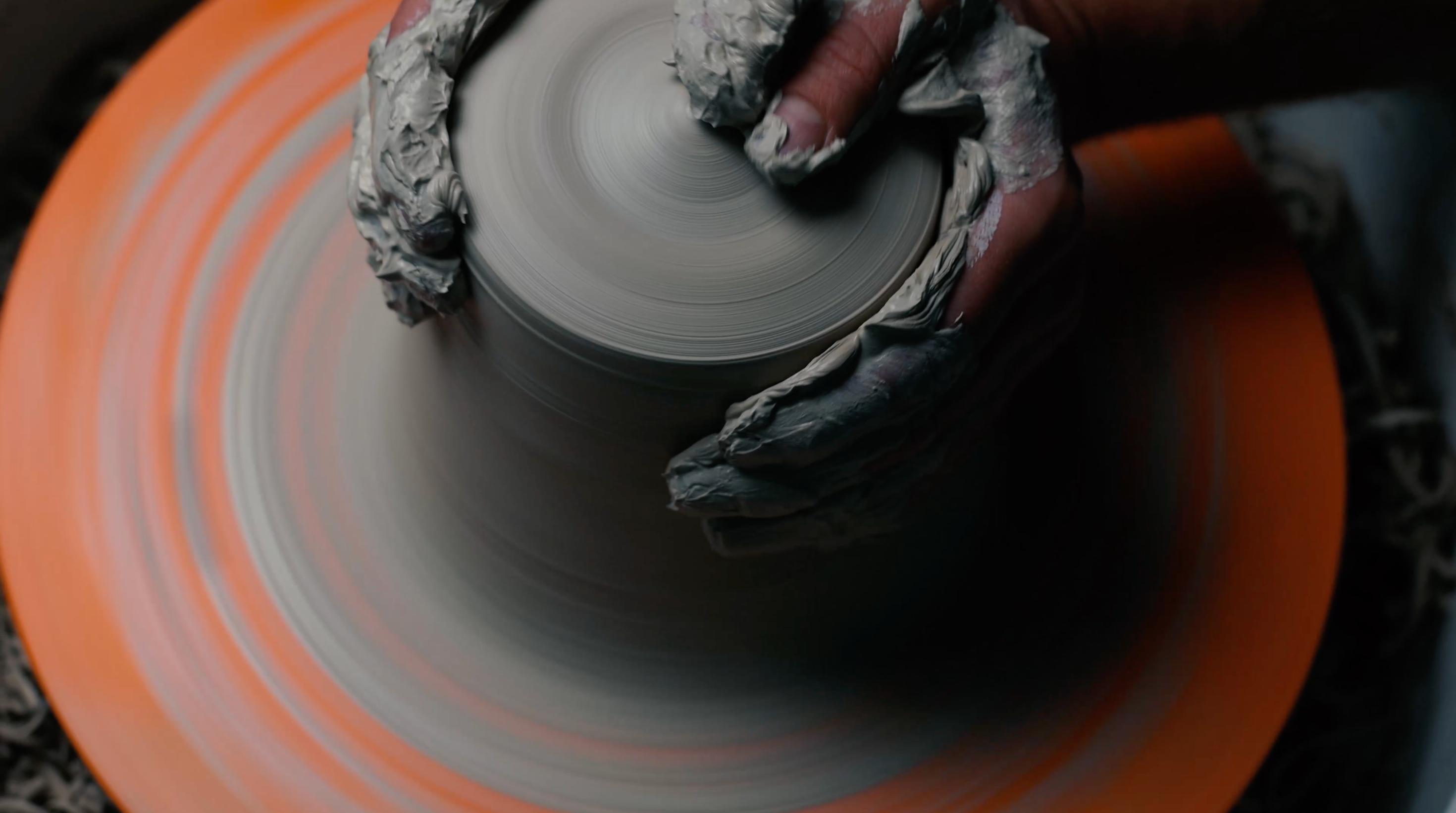 Person shaping a clay pot on a spinning wheel