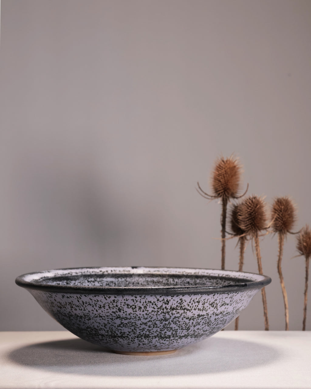 Speckled ceramic bowl on a neutral background with dried plants.