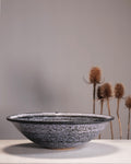 Speckled ceramic bowl on a neutral background with dried plants.