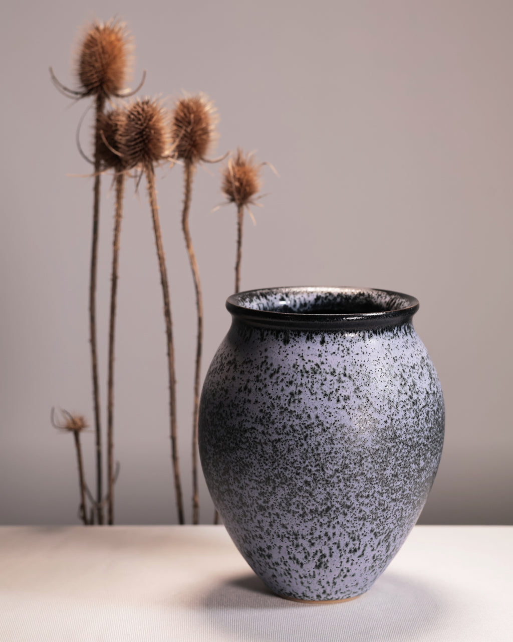 Speckled gray vase on a neutral background with dried plants.