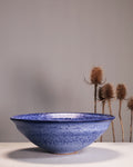 Blue ceramic bowl on a white surface with a gray background and dried plants.