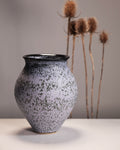 Speckled ceramic vase on a neutral background with dried plants.