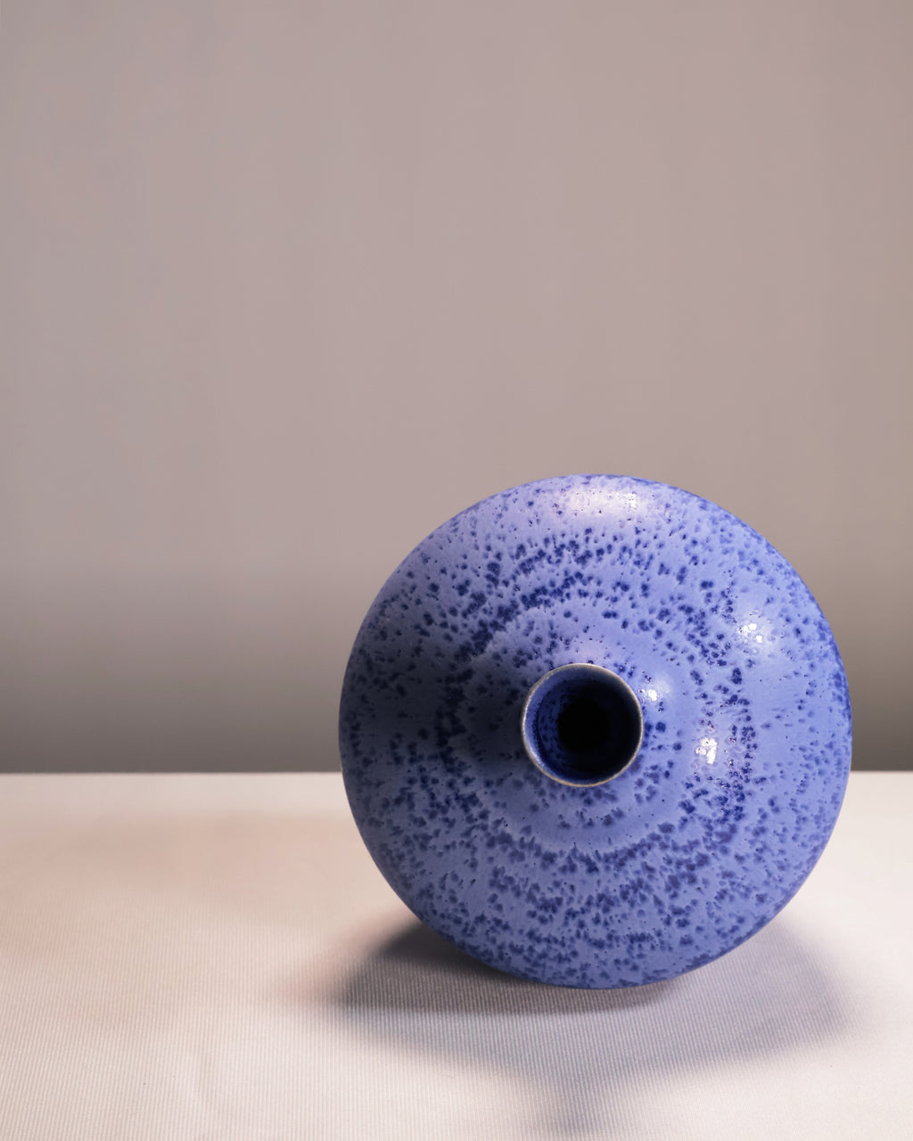 Blue speckled vase on a light surface with a gray background