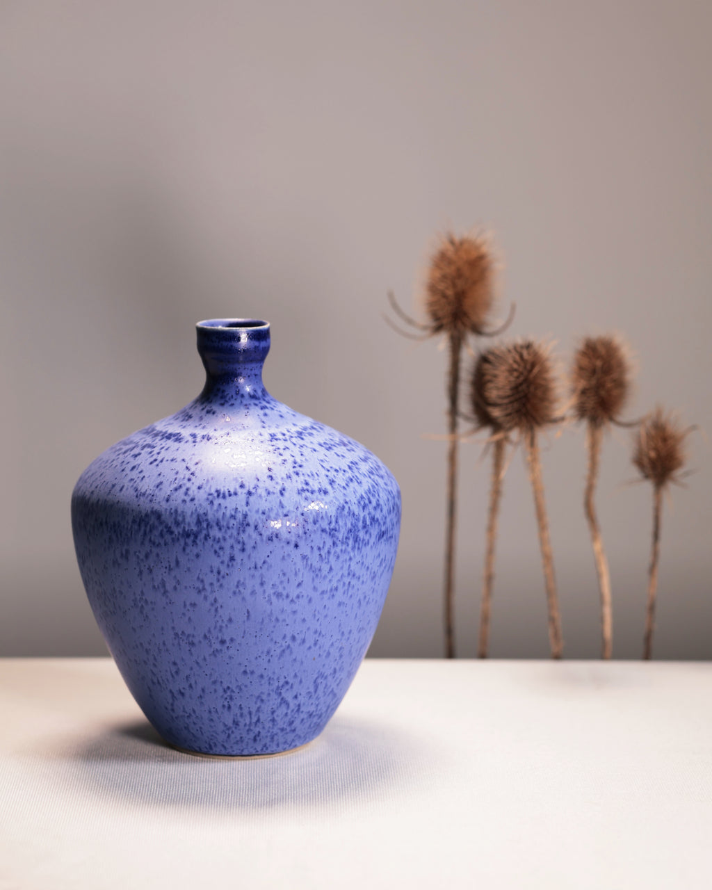 Blue speckled vase on a white surface with a neutral background